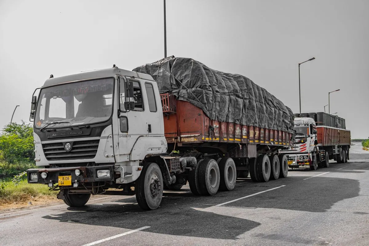Multi-axle open body truck carrying tarpaulin-covered load on an Indian expressway